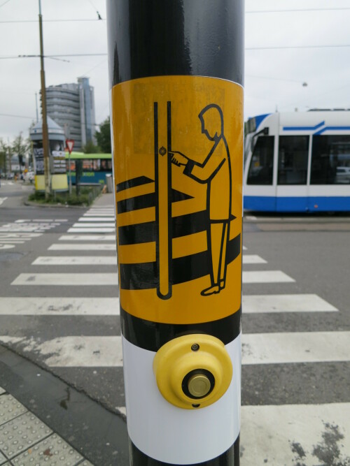 Druckknopf an einer Ampel in Amsterdam mit Aufkleber als Bedienungsanleitung.