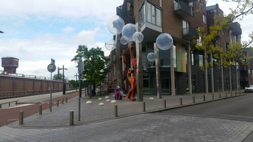 Der 13. Mai 2000 war ein schwarzer Tag in der niederländischen Stadt Enschede. Mitten im Stadtteil Roombeek explodierte die Feuerwerkfabrik S. E. Fireworks. 177 Tonnen Feuerwerkskörper legten das ganze Stadtquartier in Trümmer.

23 Menschen – darunter vier Feuerwehrmänner – starben, 947 Menschen wurden verletzt. 1.500 Wohngebäude wurden durch die Explosion beschädigt oder gerieten durch umherfliegende Feuerwerkskörper in Brand. 200 Wohnhäuser wurden vollständig zerstört und rund 300 als unbewohnbar erklärt. Darüber hinaus wurden über 100 Betriebe beschädigt. In nur einer Stunde verlieren mehr als 1.250 Einwohner ihr Zuhause.

Etwa zwei Drittel des 65 Hektar großen Stadtviertels, welches nördlich an den Hauptbahnhof und die Innenstadt anschließt, waren durch die Explosion betroffen. Mit der Katastrophe waren jedoch auch Chancen und Entwicklungspotenziale verbunden, welche einen Neuanfang für das durch die sterbende Textilindustrie geprägte Quartier bedeuten.

Der für den Wiederaufbau entwickelte Masterplan von Pi de Bruijn (de Architecten Cie. aus Amsterdam - www.cie.nl/projects/53 | Video: https://vimeo.com/51809482) verkörpert eine State of the Art-Stadtplanung. Die 1350 neu errichteten Wohnungen befinden sich in einem durchmischten Gebiet, welches durch kulturelle Angebote, Geschäfte und soziale Einrichtungen ergänzt wird. Freiräume, Wasser und Grün spielen ebenfalls eine große Rolle.

Dabei hat Pi de Bruijn den Einwohnern große Freiheit gelassen, selbst zu bestimmen, wie ihre Nachbarschaft aussehen soll. Üblicherweise macht die niederländische Stadtplanung vergleichsweise viele Vorgaben und lässt wenige Freiheiten. In Roombeek konnten rund 50 Prozent der Einwohner ihre neuen Wohngebäude vollkommen frei entwerfen, nur für die Bereiche an den Hauptverkehrsachsen wurden strengere Vorgaben gemacht. Das Straßennetz wurde exakt in der Form wieder aufgebaut, in der es vor der Explosion existierte. Dies sollte den ehemaligen Bewohnern ein rasches Ankommen und Einleben ermöglichen. Zudem wurde versucht, die vereinzelten noch stehenden Gebäude, soweit es geht, zu sichern und weiterzuentwickeln.