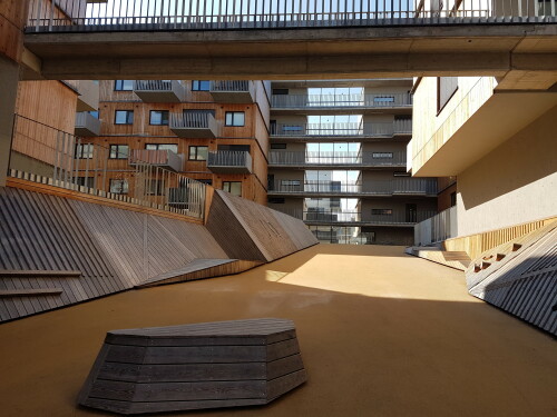 Die Gestaltung des Bauplatzes D12 in Wien Aspern steht ganz im Zeichen des Baustoffes Holz. Die aktive Zone der Wohnsiedlung ist der Begegnungsraum und Jugendspielplatz – der Canyon. Ein einheitlicher EPDM Belag trägt zum Schallschutz bei. In ihm liegen frei verteilt Holzobjekte und -flächen. Die Holzverkleidung entlang der Rampenwände wächst stellenweise aus der Wand und bildet eine schräge Fläche zum Anlehnen bzw. als Kletterwand. Große vertikale Flächen verbinden sich mit der Wand und bilden Liege- oder Nutzflächen.

Bauherrschaft: EBG Gemeinnützige Baugen. reg. m.b.H.

Architektur :querkraft architekten, Berger + Parkkinen Architekten

Die Seestadt Aspern ist eines der größten Stadtentwicklungsprojekte Europas der 2010er Jahre. Über einen Zeitraum von rund 20 Jahren soll ein neuer Stadtteil entstehen, in dem über 20.000 Menschen wohnen und arbeiten sollen. Die erste von drei Entwicklungsetappen konzentriert sich auf den Süden des Stadtteils und soll 2020 abgeschlossen sein.